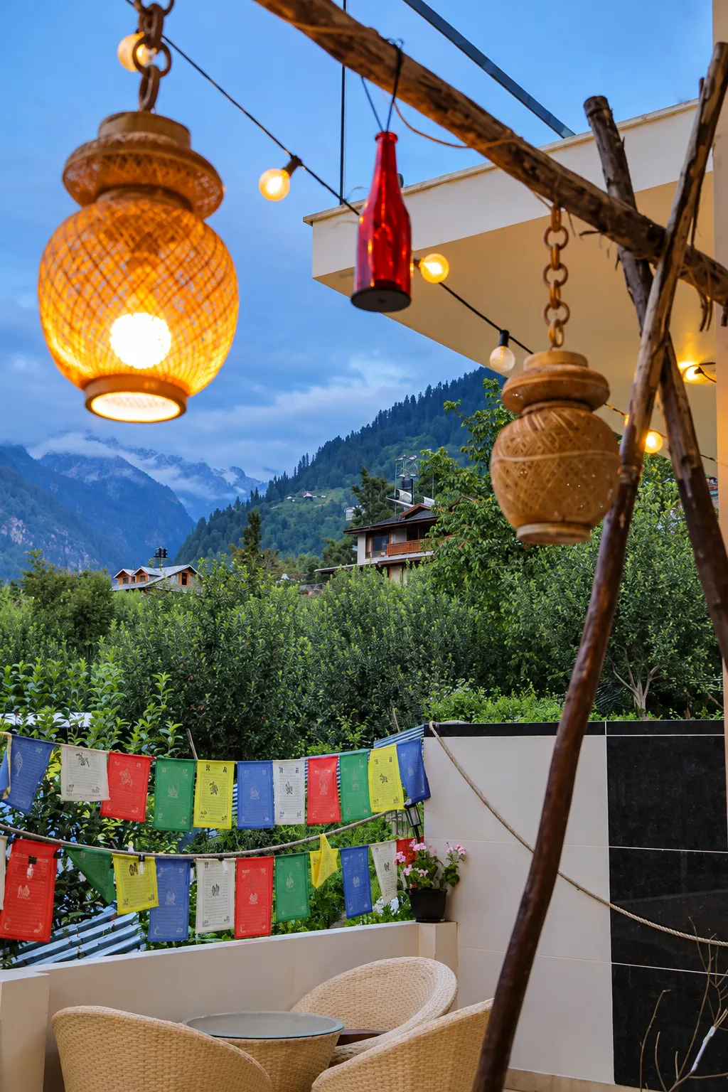 Cafe DO NTHNG terrace in Manali at dusk, with glowing bamboo lanterns, prayer flags and mountain views
