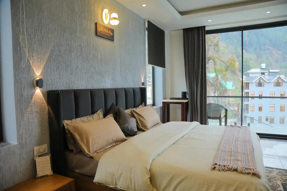 Bedroom with a grey headboard wall, wall lights and a large window overlooking the hillside and nearby buildings