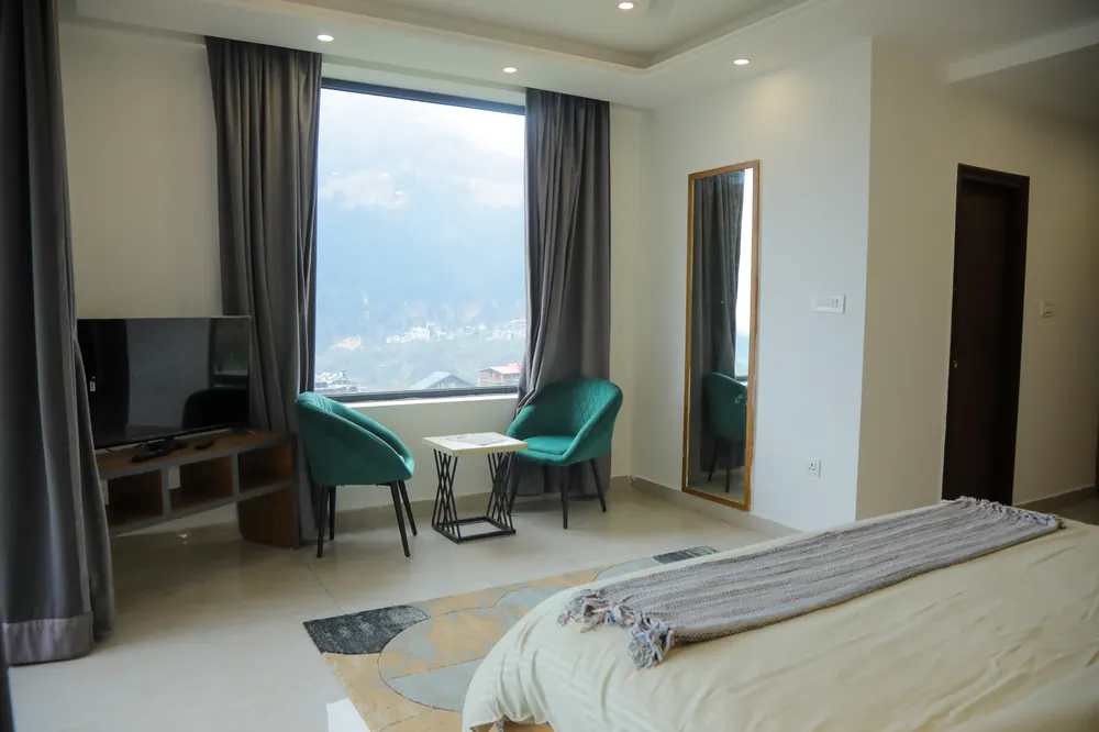 Bedroom with a window onto the mountains, two teal armchairs, a small table and a television unit